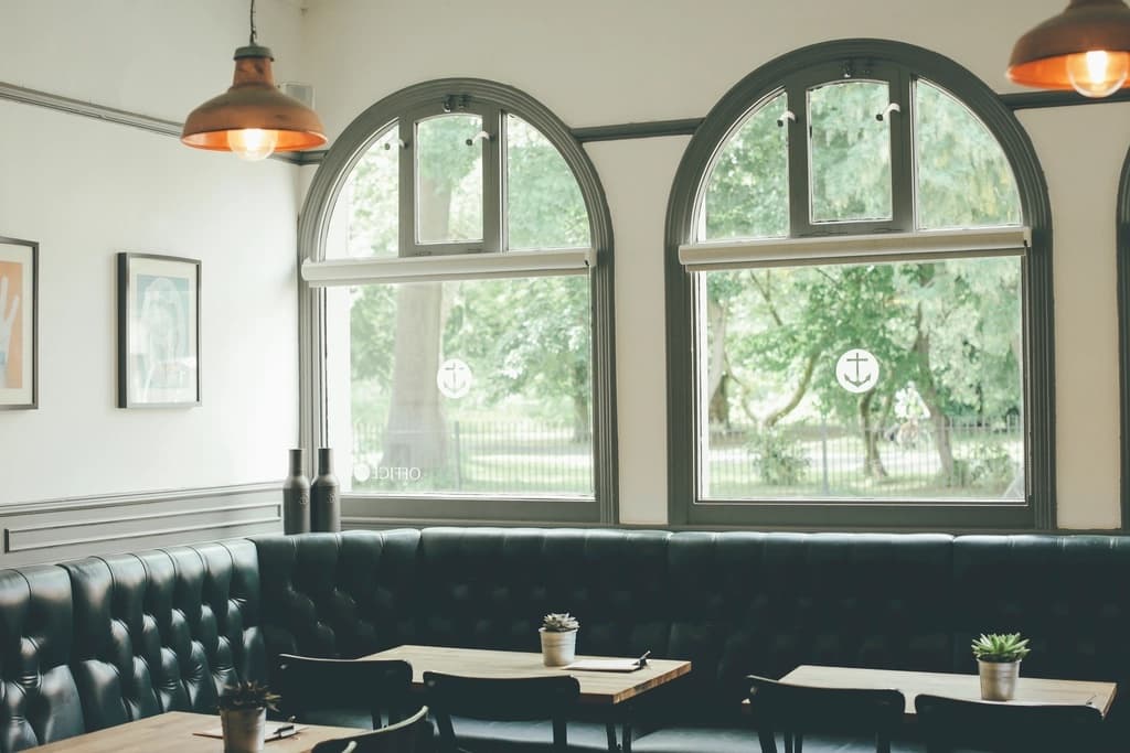 Arched windows and deep green banquettes inside a bright, elegant cafe