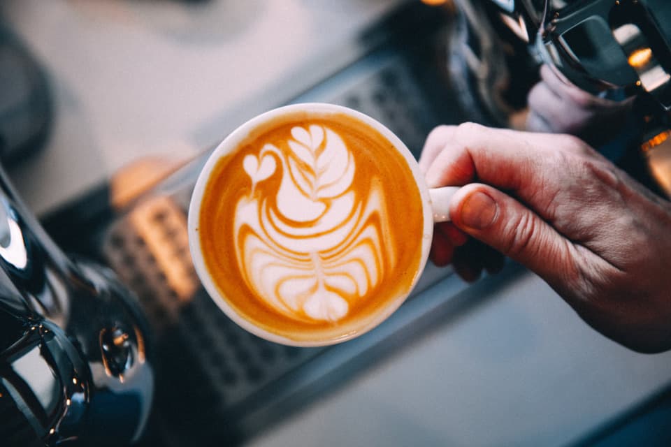 A barista holding a cup of coffee with leaf latte art