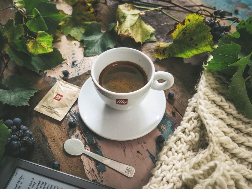 An espresso on a wooden table surrounded by leaves