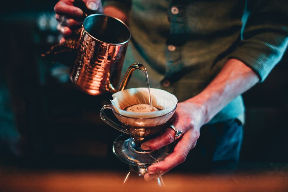 A barista slowly pouring water over coffee grounds