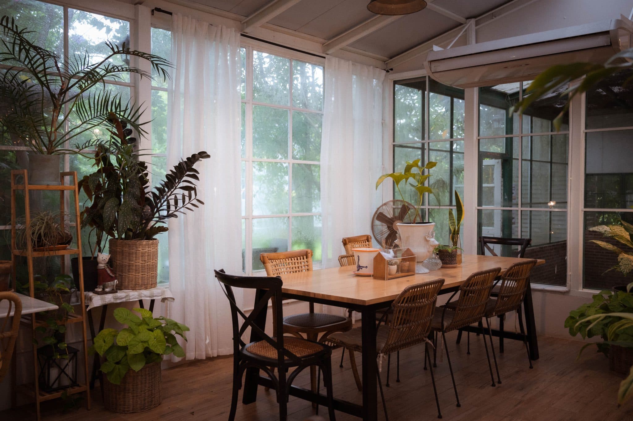 A sunlit dining room filled with plants and wooden tables